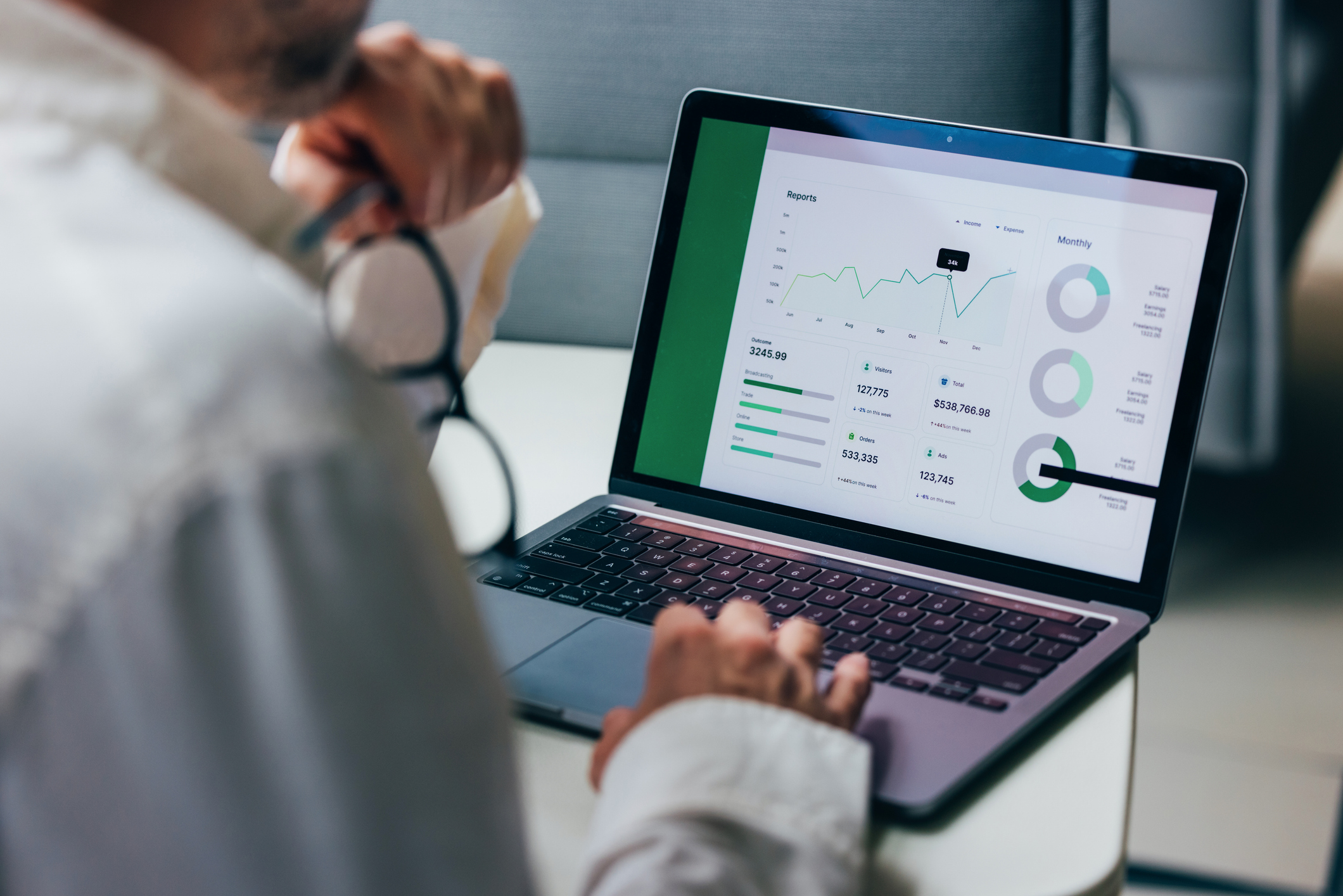 A professional focuses on analyzing detailed business reports displayed on a laptop screen. The graphics include various charts and performance metrics, highlighting statistical trends for comprehensive decision-making in a corporate environment.